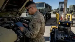 Service member inspecting vehicle engine outdoors