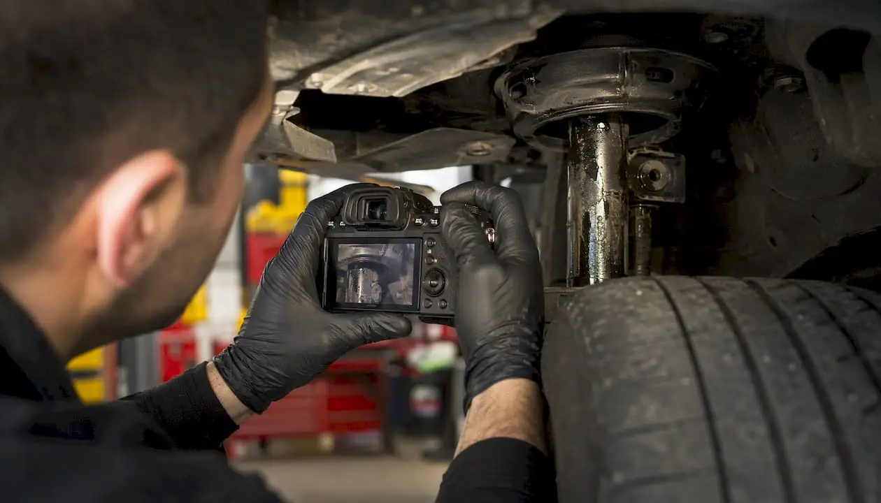 Technician photographing worn strut and cupped tire