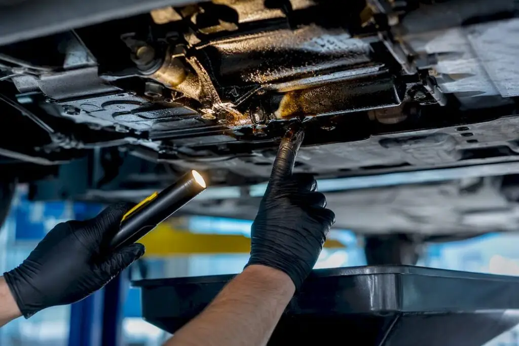 Technician inspecting oil leak under vehicle