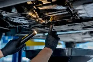Technician inspecting oil leak under vehicle
